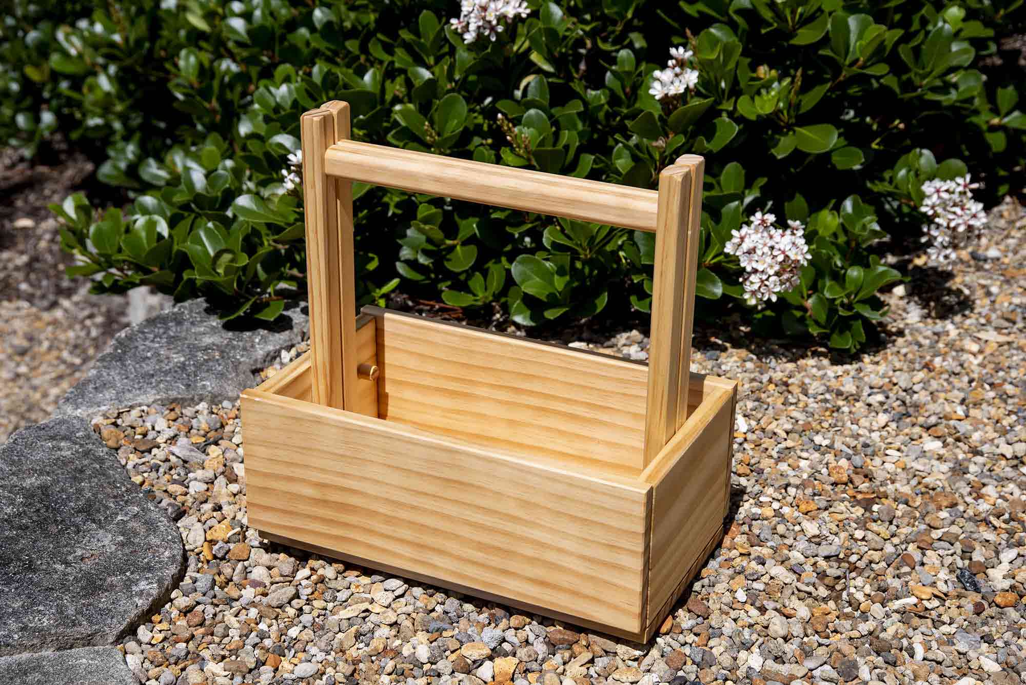 Wooden tool carrier on a gravel surface with greenery in the background. Victoria James Home Storage Box VJA Convertible