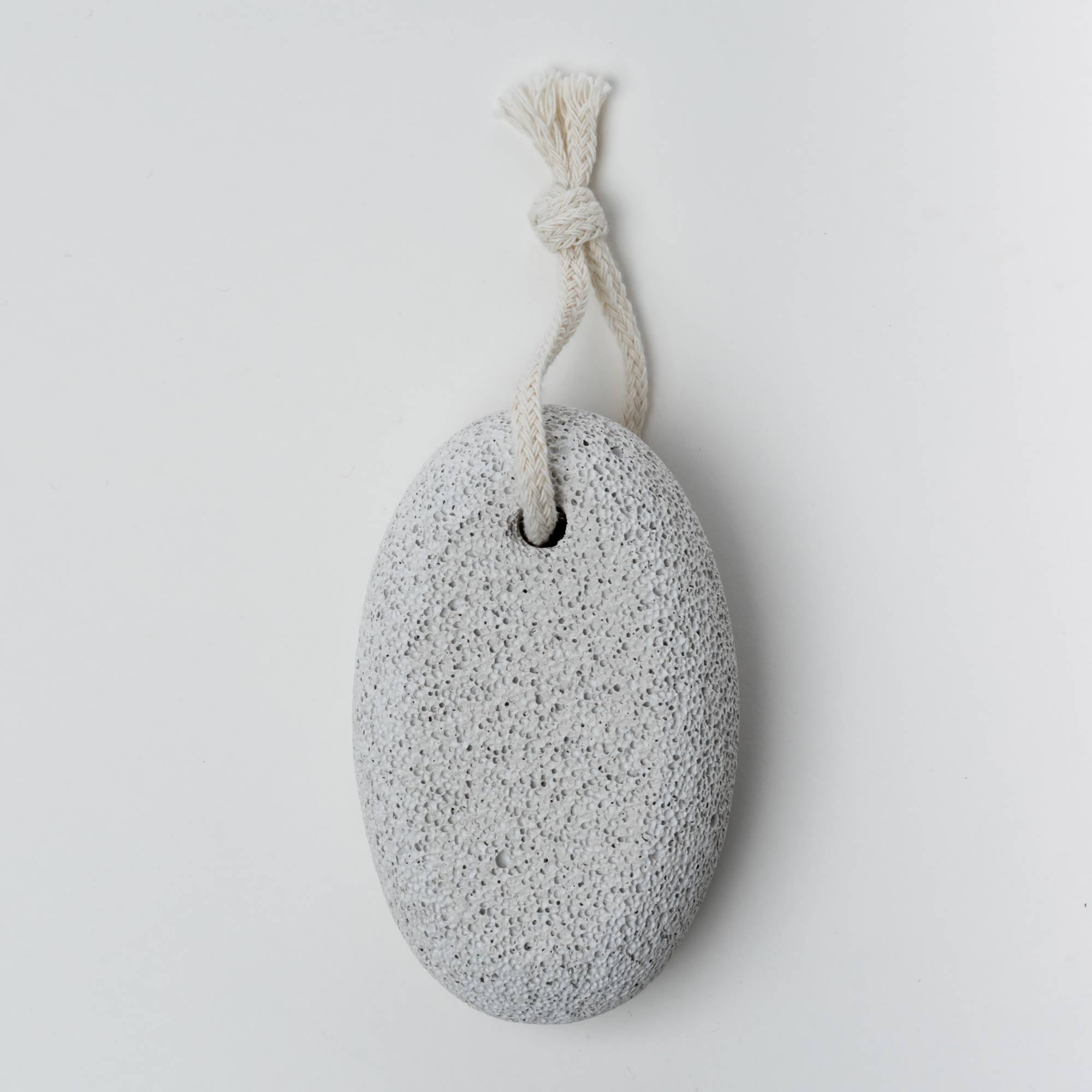 Oval-shaped pumice stone with a rope on a light gray background. Victoria James Body Pumice Stone
