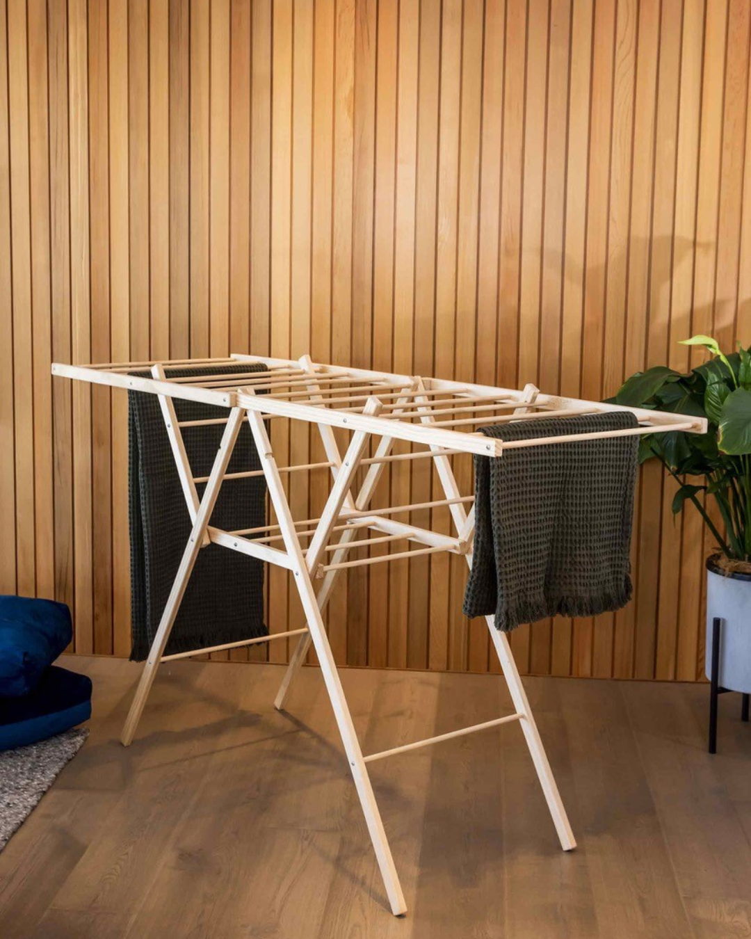 Wooden drying rack with clothes against a wooden wall. Simply Clean Victoria James Eco Clothes Airer