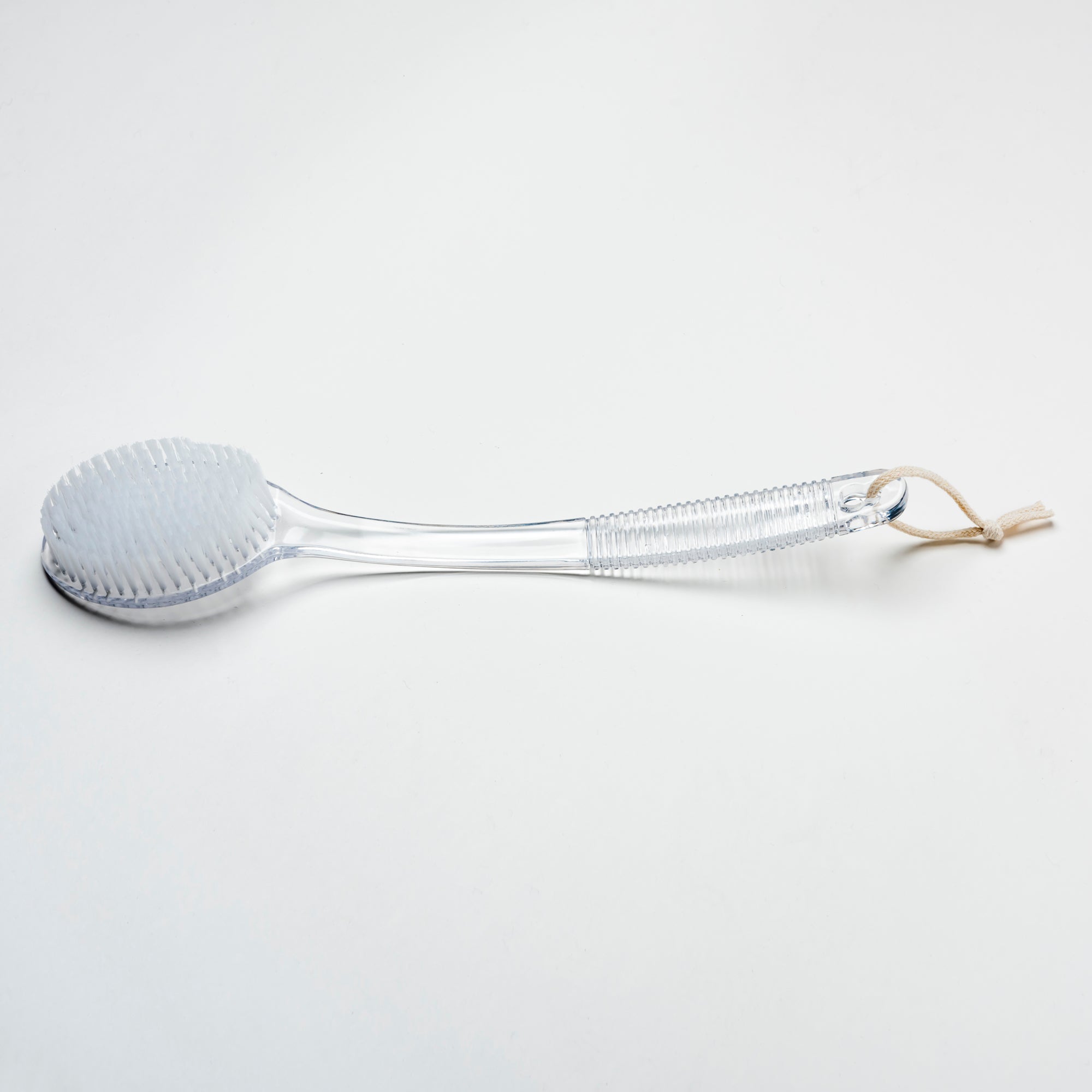 Clear bath brush with a rope handle on a light gray background. Victoria James Body Bath & Shower Brush