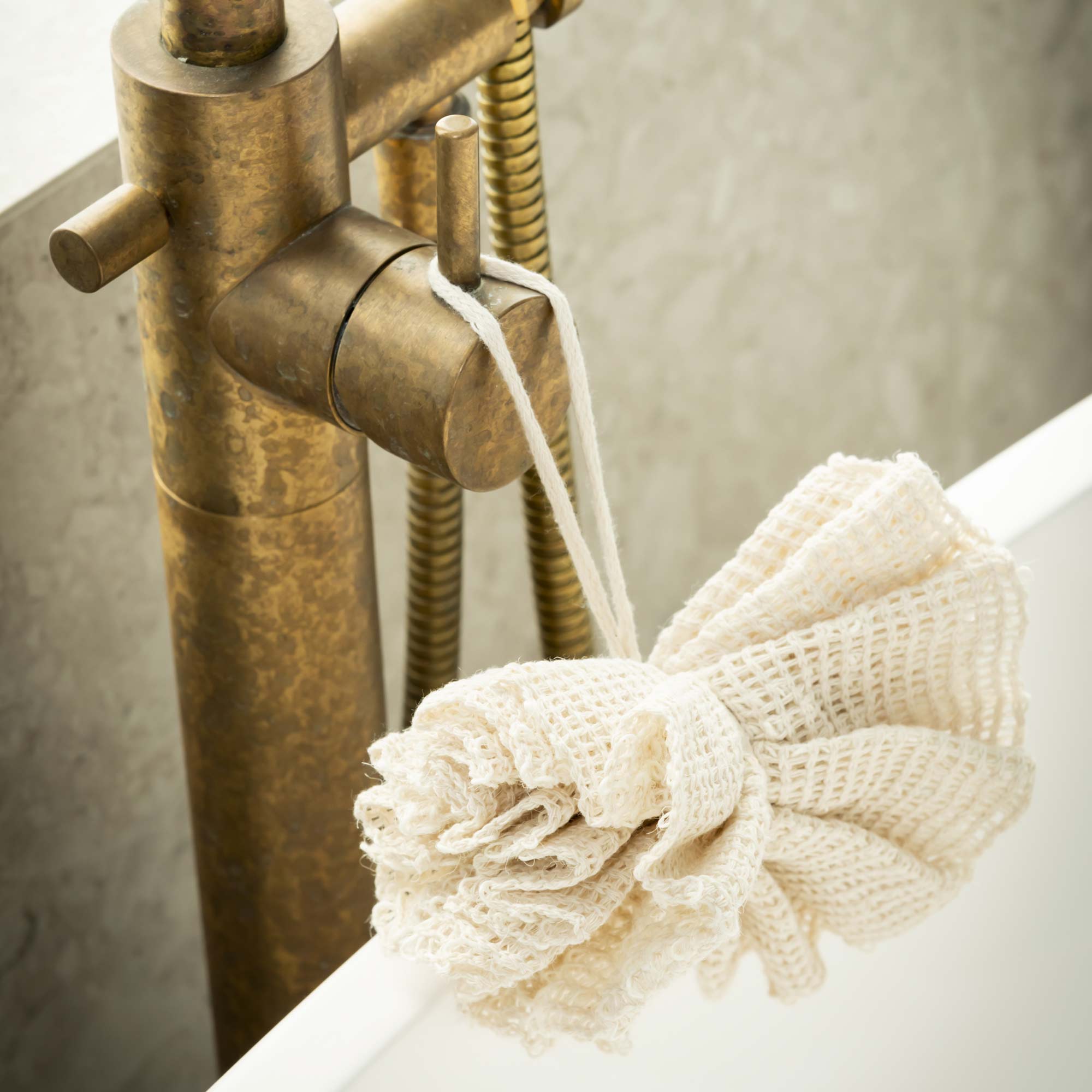Close-up of a brass faucet with a white bath mat and towel on a bathtub. Victoria James Body Ramie Bath Puff