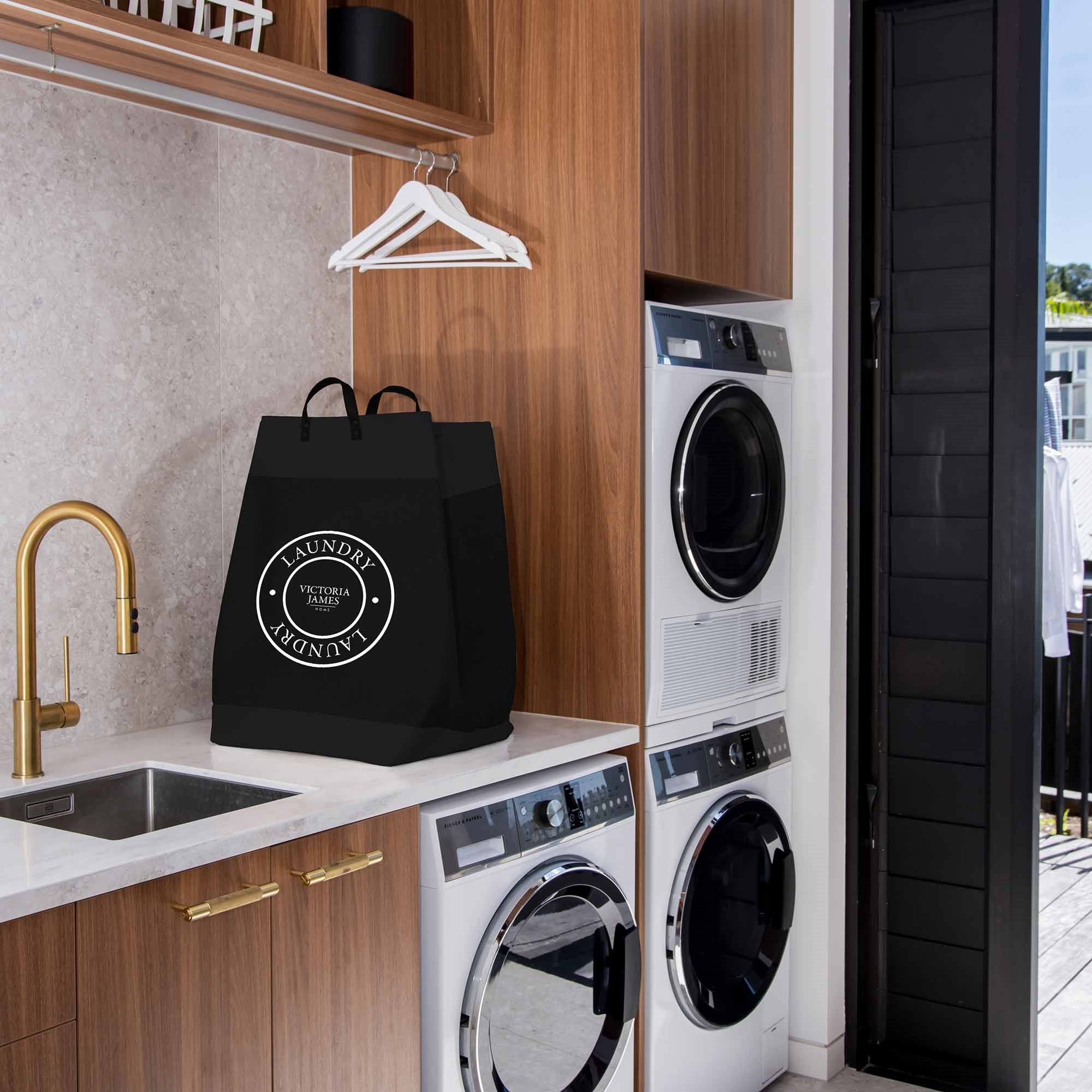 Laundry room with washing machines, a black bag labeled 'Laundry', and wooden cabinets. Victoria James Home Laundry Hamper
