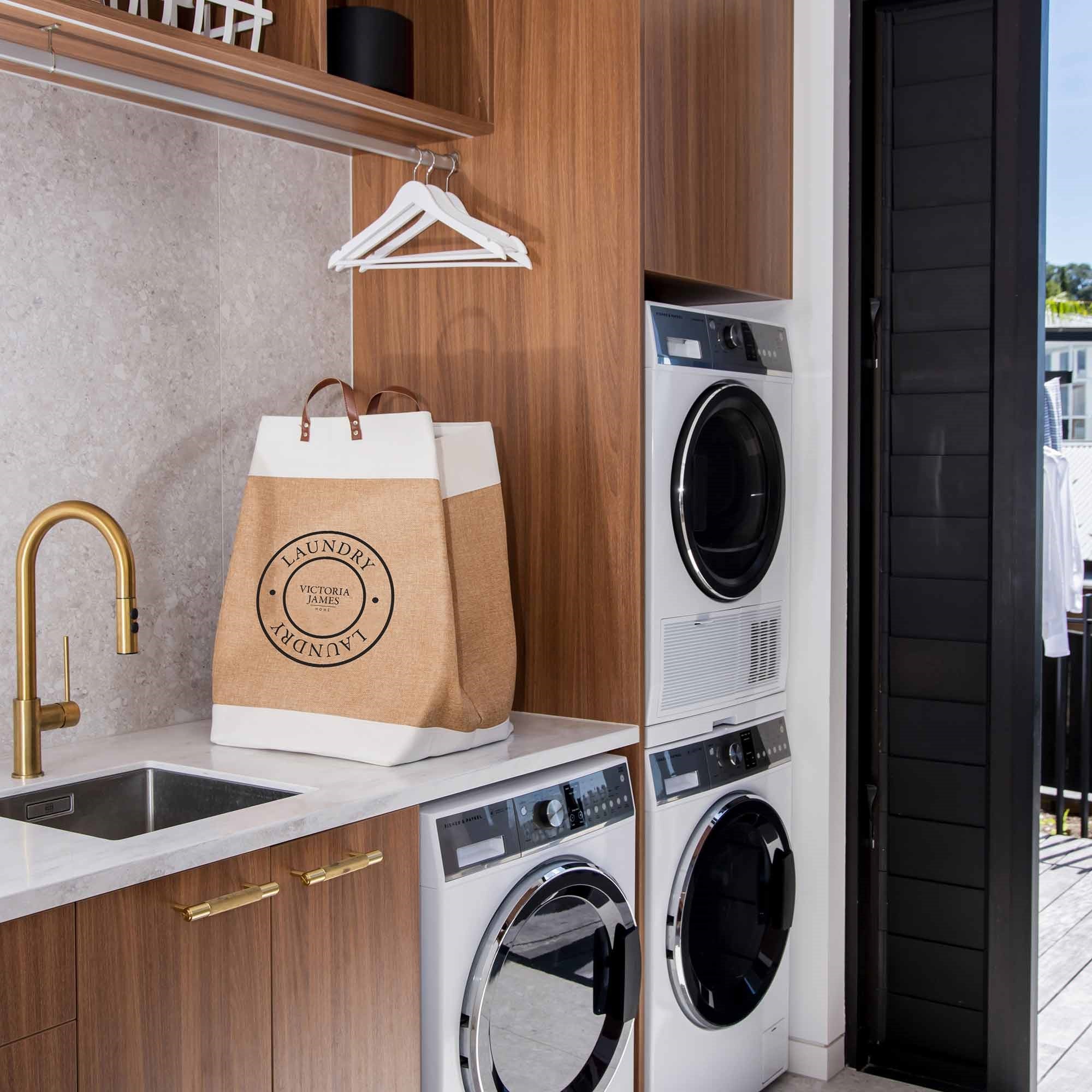 Laundry room with washer, dryer, and a 'Laundry' bag on a counter. Victoria James Home Laundry Hamper